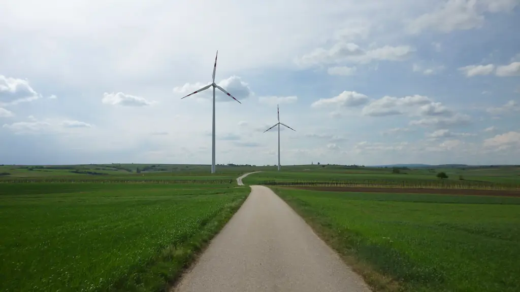 Road through green fields towards a wind turbine